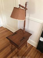 Vintage wooden telephone table with attached lamp, showing hinged top, turned legs, and fabric lampshade.