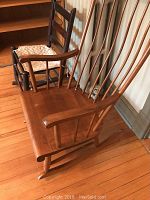 Wooden Windsor style rocking chair with spindled back, armrests, and curved rockers showing some wear on seat and paint on rockers.