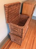 Photo of two woven wicker baskets, one open showing interior and one closed, positioned stacked corner against wall.