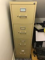 Front view of beige metal filing cabinet with four drawers, showing wear and scratches.