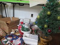 Photo showing small decorated Christmas tree on gold motorized base, assorted Christmas items including place mats and box in background