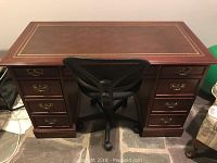 Full front view of the wood sleigh style desk showing inlay top and drawer hardware, positioned on stone floor.