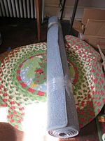 Round Christmas themed braided rug lying flat with rolled blue rug on top