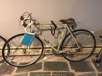 Full side view of the white Univega Gran Primo steel road bike with drop handlebars, brown saddle, and 27-inch wheels on stone floor.