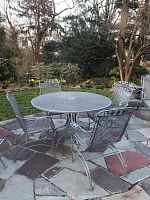 Overall view of round mesh table and four rocking chairs on stone patio