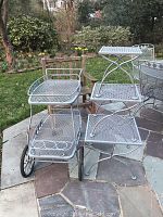 Photo showing the wrought iron tea cart and three wrought iron tables of various sizes outdoors with some rust visible