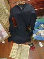 Two navy World War II naval jackets displayed with pants, patch, and historic newspaper on floor