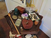 Overview of men's collectible items including blue Hemingray glass insulator, wooden plaque clock, belt buckle, sunglasses, keys, walking stick, and various small objects placed on a wooden stand.