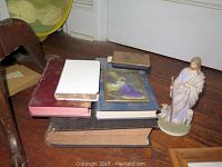 Full view of all items including Bibles stacked with a framed print and Jesus figurine on a wooden floor