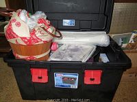 Black plastic Sterilite storage container filled with rolls of backing fabric, spray adhesive, sewing basket with fabric, and various sewing supplies.