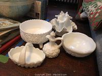 Photo showing assortment of milk glass items on a table including bowls, basket, cruet bottle, and bud vase