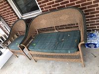 View of the loveseat and matching chair outdoors on a concrete porch against a brick wall, showing their overall structure and cushions with visible dirt and soiling.