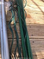 Close-up photo showing both straight plastic green garden stakes and curved green metal garden stakes on a wooden surface.
