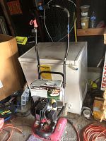 overall view of red Troy-Bilt tiller leaning against chest freezer with Craftsman grass shears box attached to handle