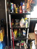 Black plastic shelving unit holding assorted household and painting supplies with fishing rod attached to the side.