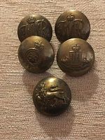 Photo showing five vintage brass military buttons with various crowned emblems and monograms including 'GR', crowned lion, and other heraldic symbols.