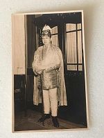 Front of the postcard showing a man wearing a metallic costume with helmet and cape indoors.