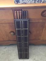 Tall dark stained wooden cribbage board with six pegs shown leaning against a wooden cabinet.