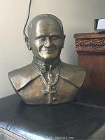 Front and three-quarter view of bronze-colored bust of Pope John Paul II, showing details of the face, cross necklace, and slight chip on the nose.