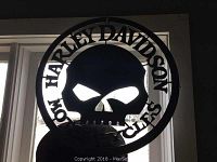 Front view of black metal circular wall hanger with skull and Harley Davidson text.