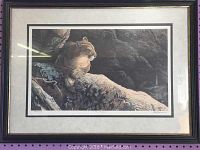Framed print of a mountain lion on a rock with a dark wooden frame and beige matting, shown front view.