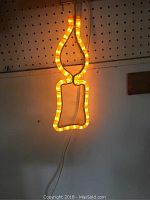 Photo of illuminated beer bottle-shaped light mounted on pegboard showing full shape and lit glow.