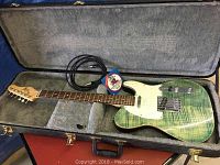 Guitar in open hardshell case with instrument cable and pack of extra strings