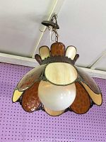 Front view of vintage hanging light fixture showing amber and cream stained glass panels with central frosted globe bulb cover
