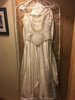 Full view of ivory satin vintage wedding dress hanging in plastic cover, sleeveless with spaghetti straps.