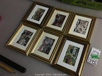 Set of 6 framed village scene prints arranged in two rows on a fabric surface. Each print is approximately 7x9 inches, with a golden frame and white matting.