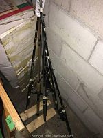 Multiple fishing rods standing upright, leaning against a concrete wall and cardboard boxes, showing handles and attached reels.