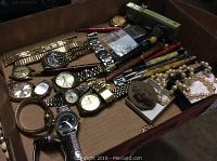 Overview of lot showing multiple wristwatches, pencils, pens and pearl necklace in cardboard tray
