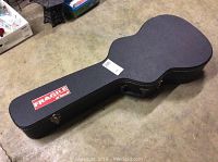 Closed black hard shell guitar case with 'Fragile' label visible on top, placed on concrete floor.