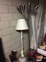 Overview of two floor lamps placed against a cinderblock wall, showing the white lamp with cherub base and floral shade alongside the metallic five-shade lamp.