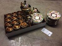 Full set in cardboard box with teapot, creamer, sugar bowl, 12 teacups with a gold interior, and 12 floral gold-accented saucers stacked outside box.