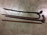 Four wooden walking sticks, including a textured dark wood cane, two straight wooden canes, and one with a curved handle and drink compartment.