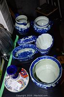 Top view of the blue and white ceramic collection on a table including bed pan, pitcher, bean pot, butter dish, and other items