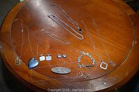 Photo showing overall lot laid out on a wooden table including necklaces, bracelets, cufflinks, and a pin.
