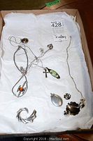 Photo of the full lot showing various necklaces with pendants, a brooch, and earrings arranged on white tissue paper inside a box.