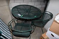 Photo of green metal round patio table with mesh design and two matching chairs.