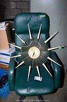 Full view of the vintage starburst wall clock placed on green leather chair showing the overall shape and size.