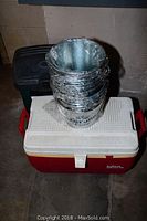Photo of stacked 13 Corona metal buckets on top of a red and white Igloo cooler with black garbage container in the background