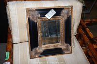 Full view of the square mirror resting on a beige fabric chair, showing the overall frame and size.