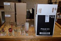 Photo showing seven beer mugs and glasses on a wooden table with packaging boxes behind them.