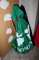 Group photo of three patio umbrellas standing closed against a wall. One is green with white design, two are dark colored (blue and red).