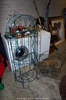 Photo shows the tall shelving unit alongside the decorative table against a background of a washer and brick wall with other items nearby.