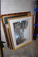 Four framed prints leaned against a wall in storage, showing varying ornate and simple frames initially stacked