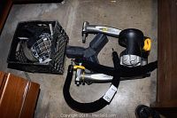 Cyclops Power handheld exercise device, black and silver with yellow knobs, alongside a crate containing a black hockey goalie mask with metal cage and some adjustable weights.