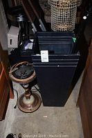 Full view of black metal rectangular container and vintage ashtray stand with black glass ashtray bowl on top.