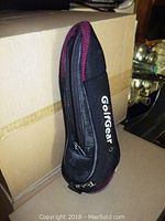 Black GolfGear golf club headcover with zipper and maroon accents, standing upright against a box.